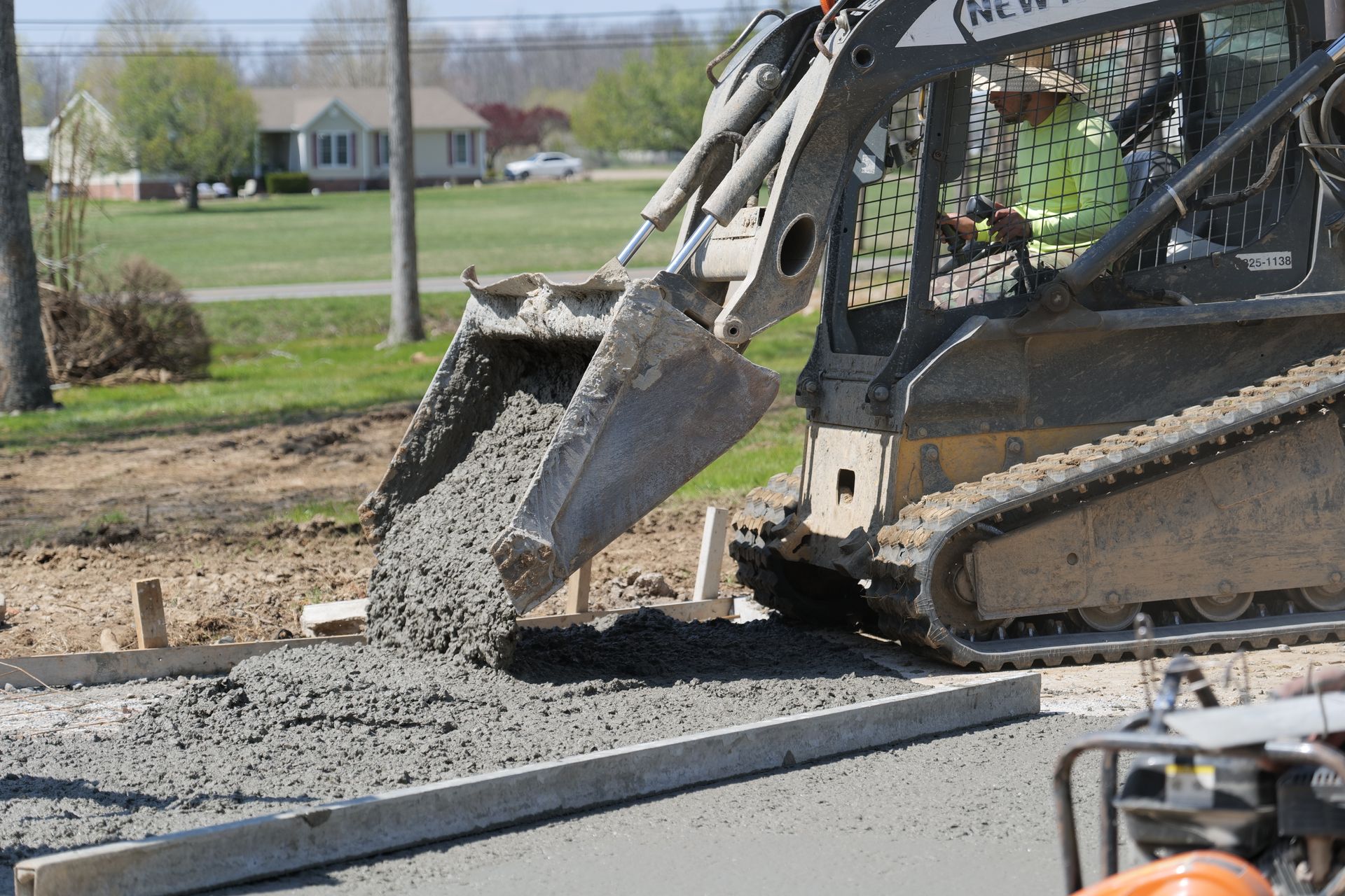 A bulldozer is pouring concrete on a driveway.