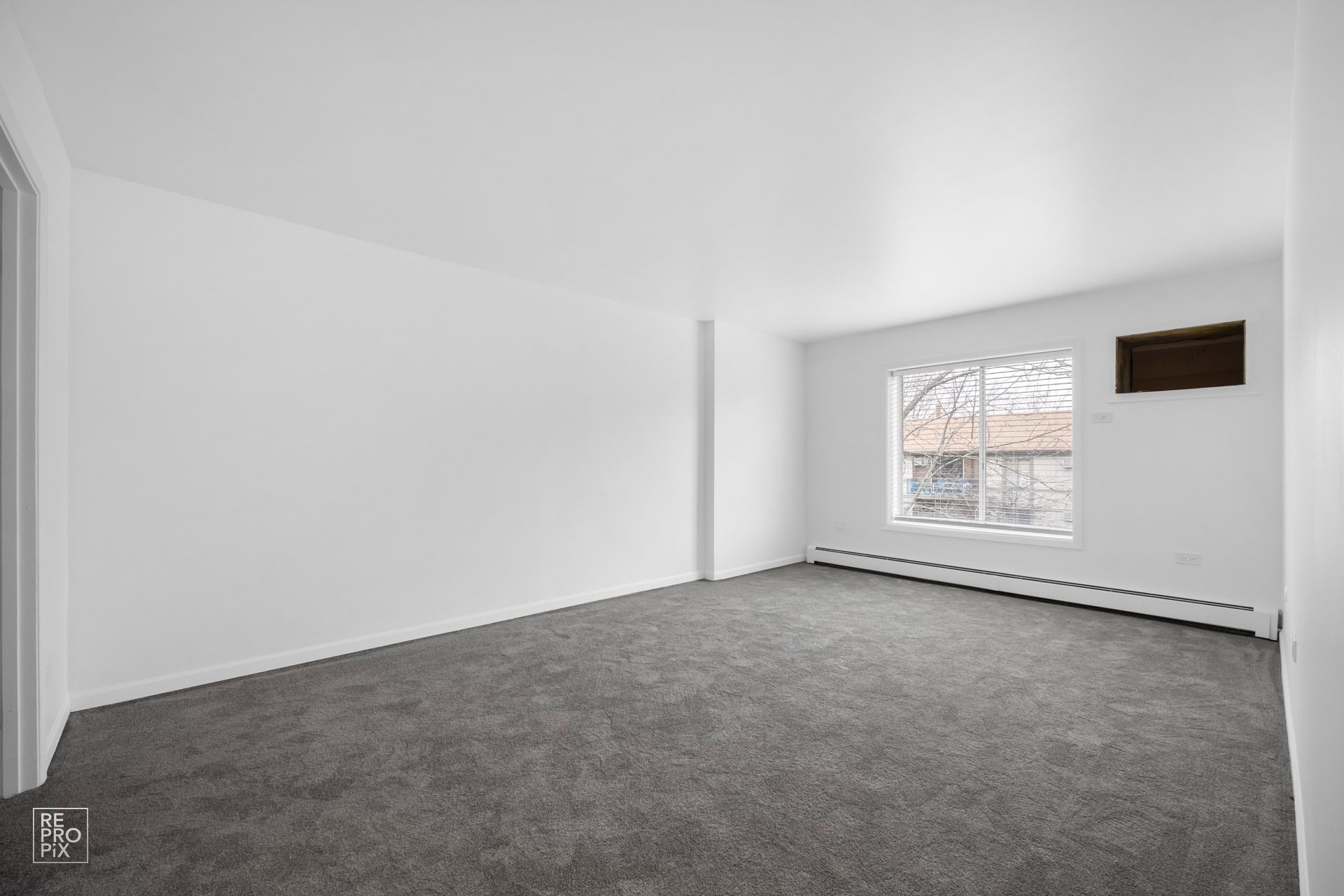 An empty living room with a gray carpet and white walls.