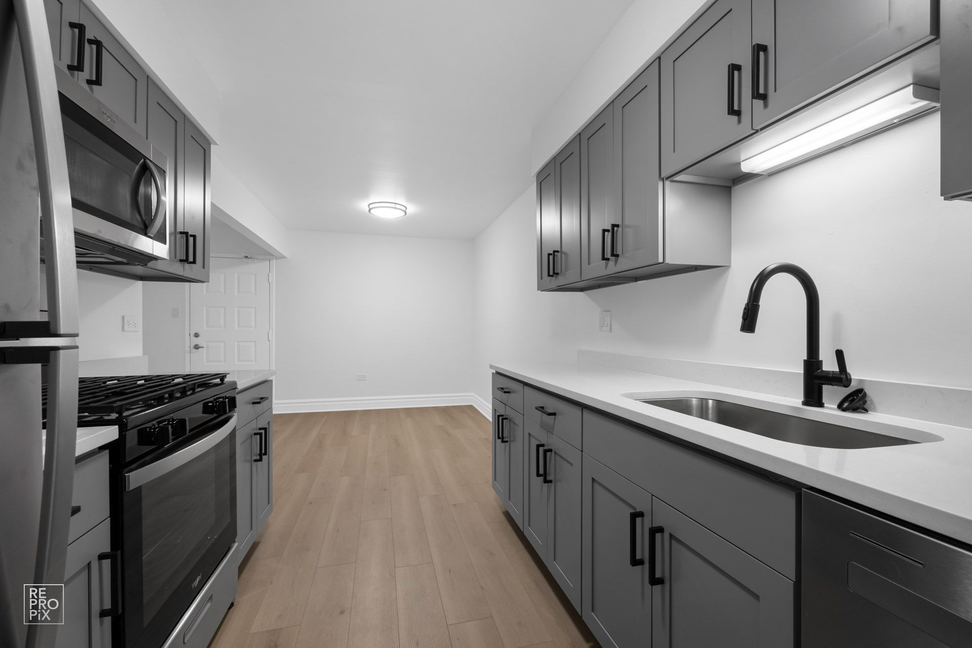 A kitchen with stainless steel appliances and gray cabinets.