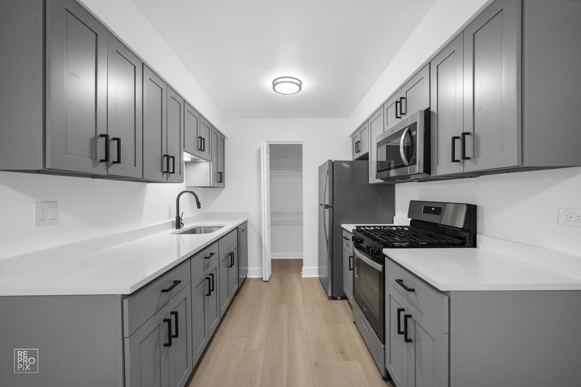 A kitchen with gray cabinets , white counter tops , stainless steel appliances and a refrigerator.