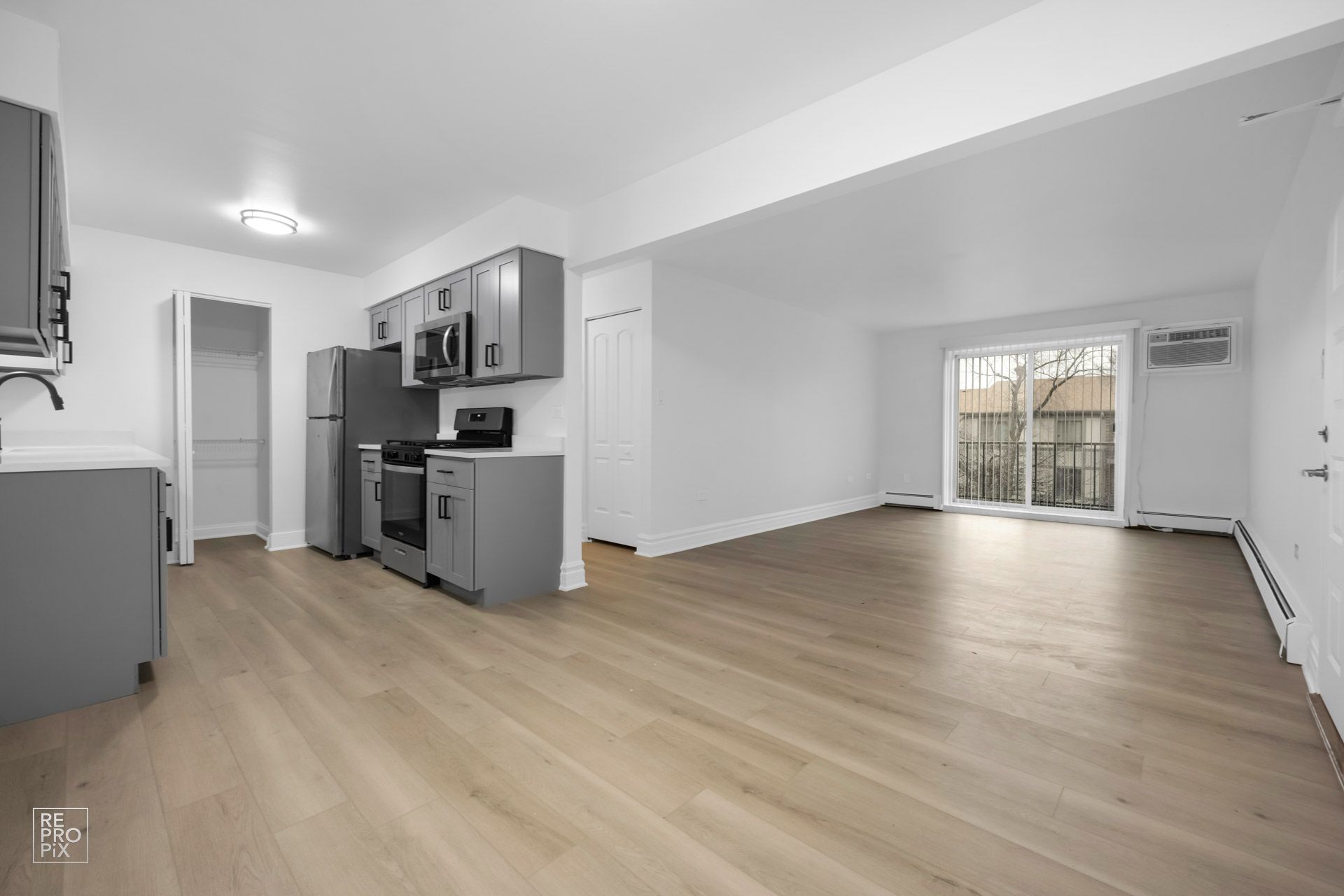 An empty apartment with a kitchen , living room , and sliding glass doors.