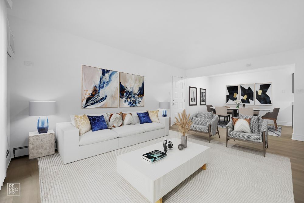 A living room with a white couch , chairs , coffee table and paintings on the wall.