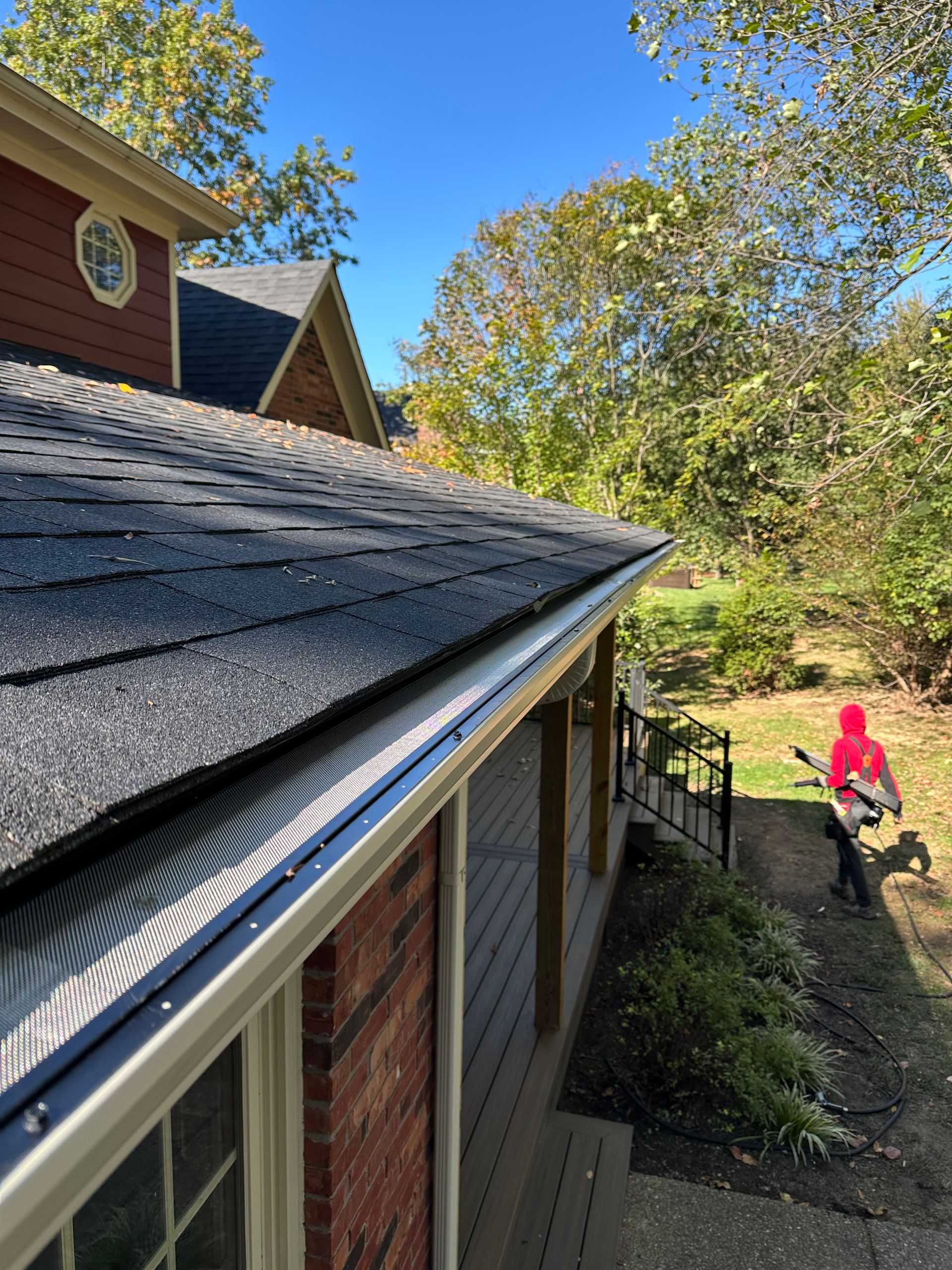 Roof edge over backyard with red-clad person walking near a fence and trees