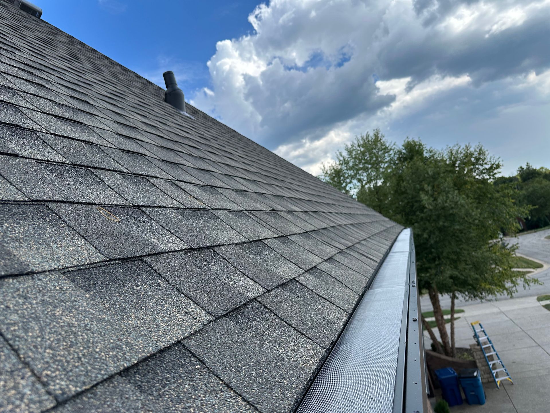 Dark gray shingle roof with a silver gutter against a cloudy sky.