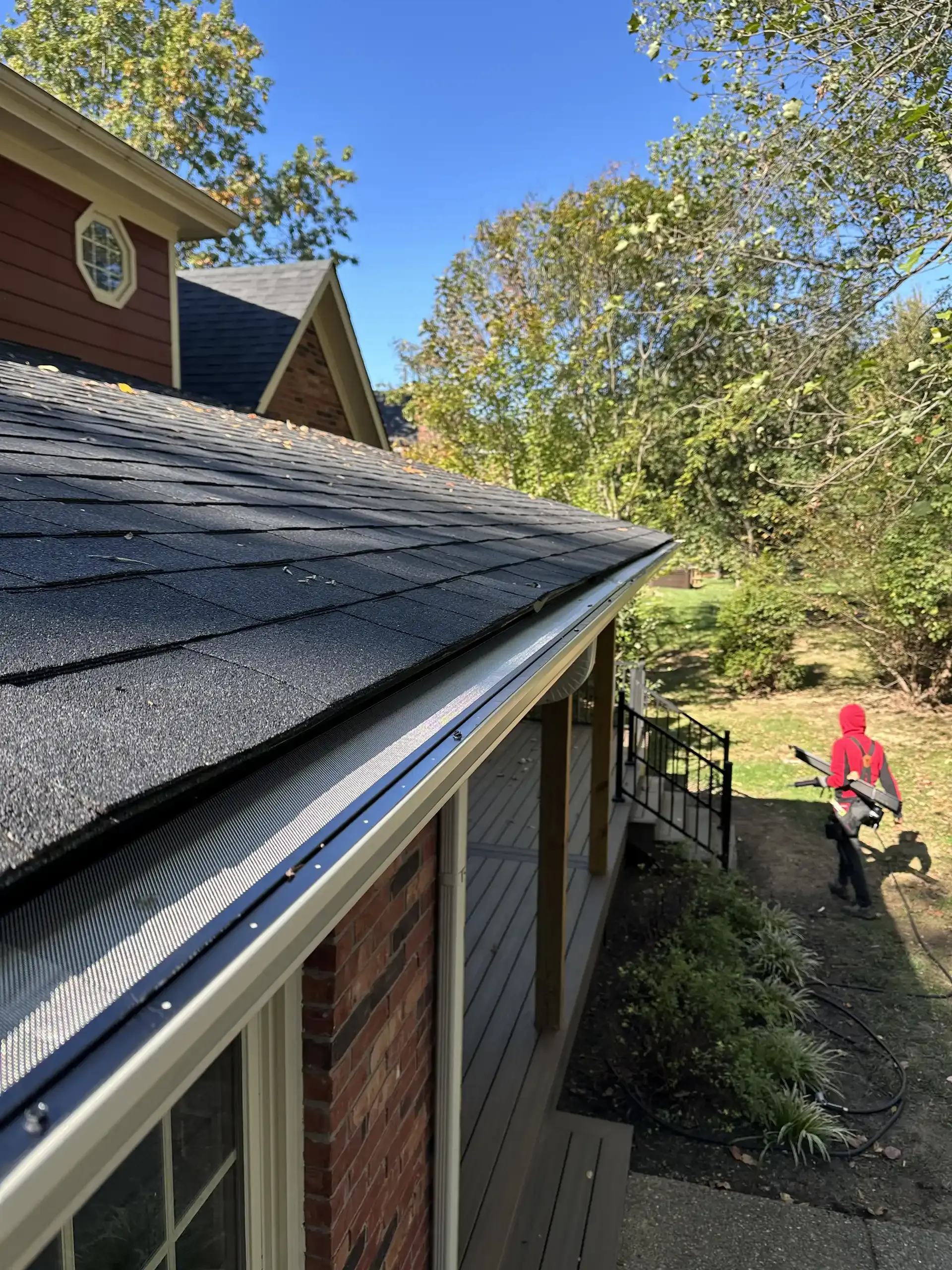 Black roof with gutter guard, a person blowing leaves with a blower in yard.