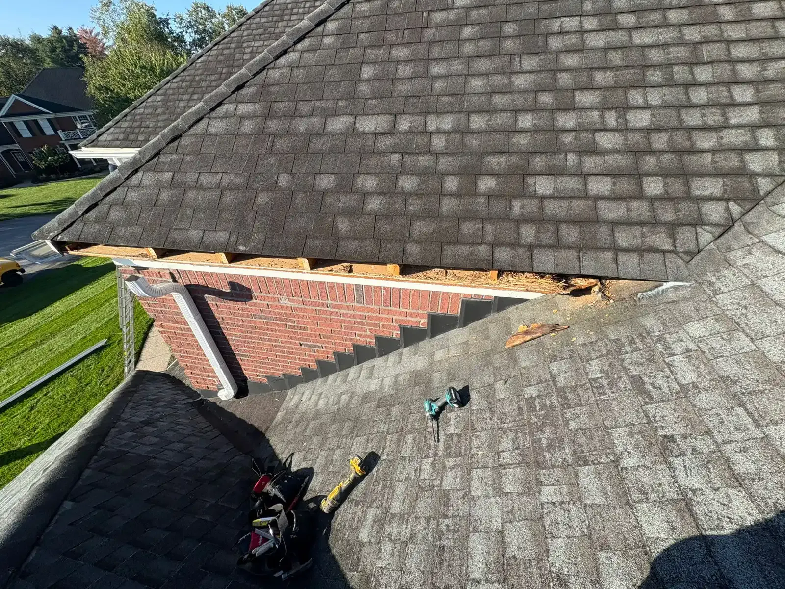 Damaged roof with missing shingles exposing brick and wood; tools lie nearby.
