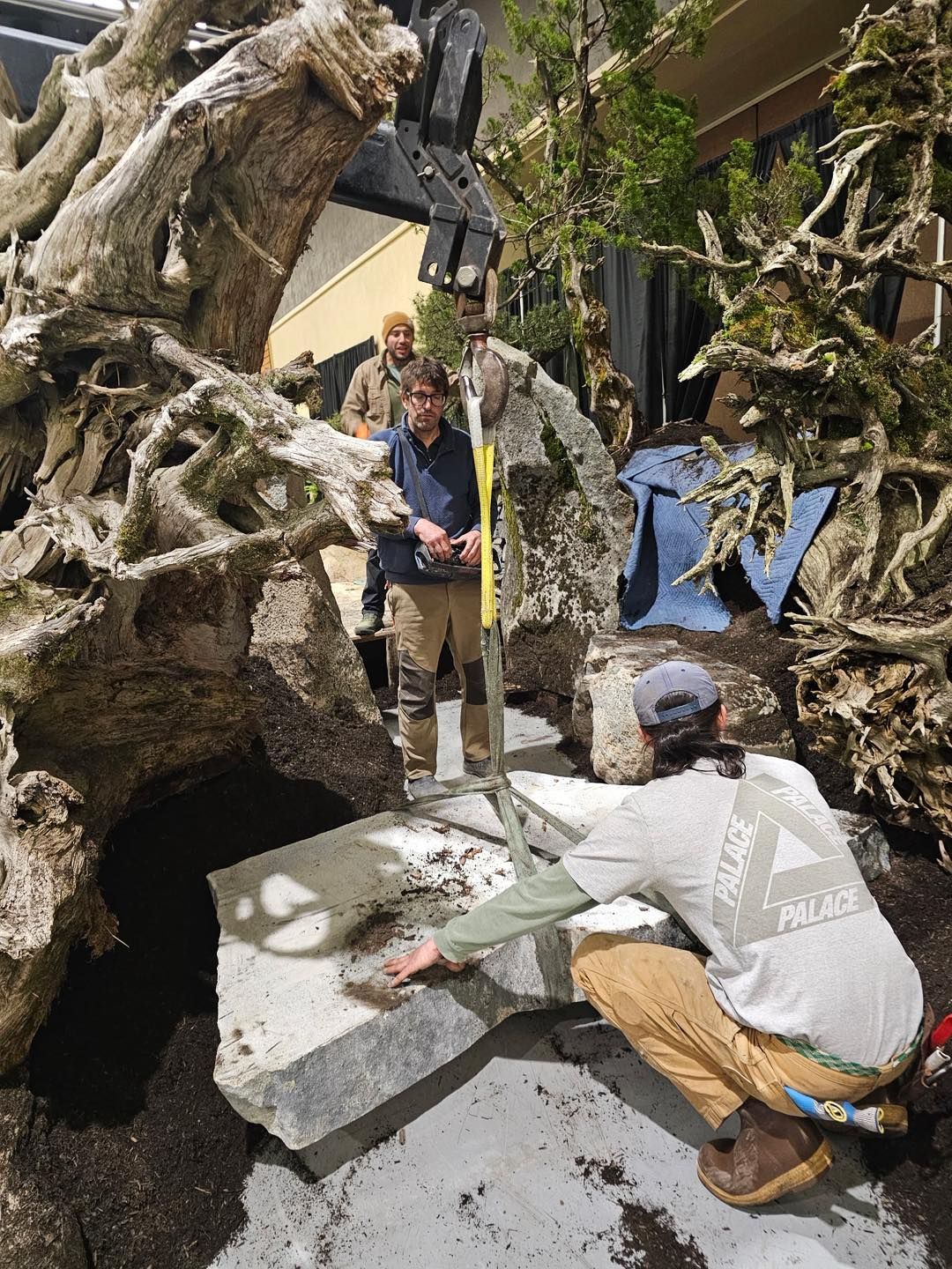 Workers clear debris from a collapsed concrete structure with a yellow measuring pole and rubble in the foreground.