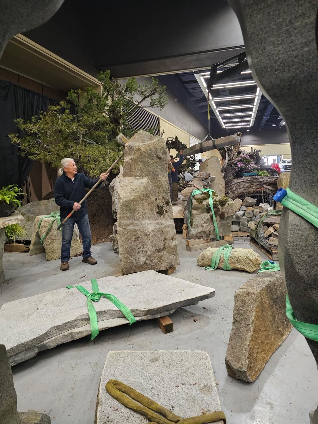 Stone exhibit with large carved rocks, a person holding a tool, and wrapped artifacts in a museum hall