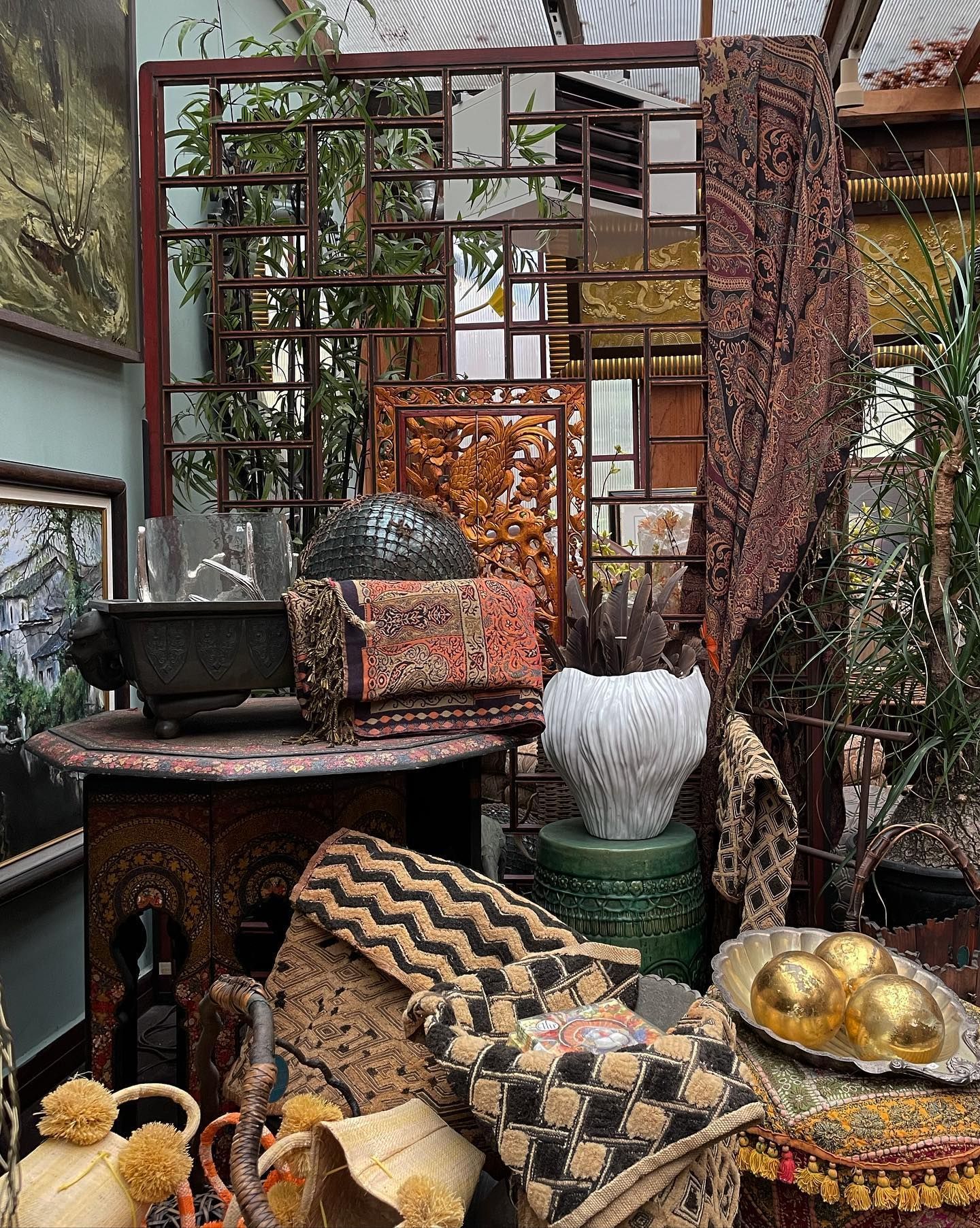 Outdoor display of patterned cushions, carved furniture, and decorative metal screens in a rustic courtyard