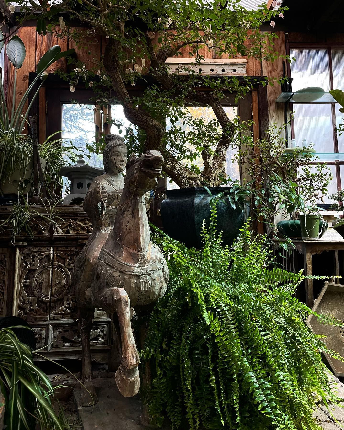 Rustic garden courtyard with a weathered statue, lush ferns, and ivy-covered brick walls.