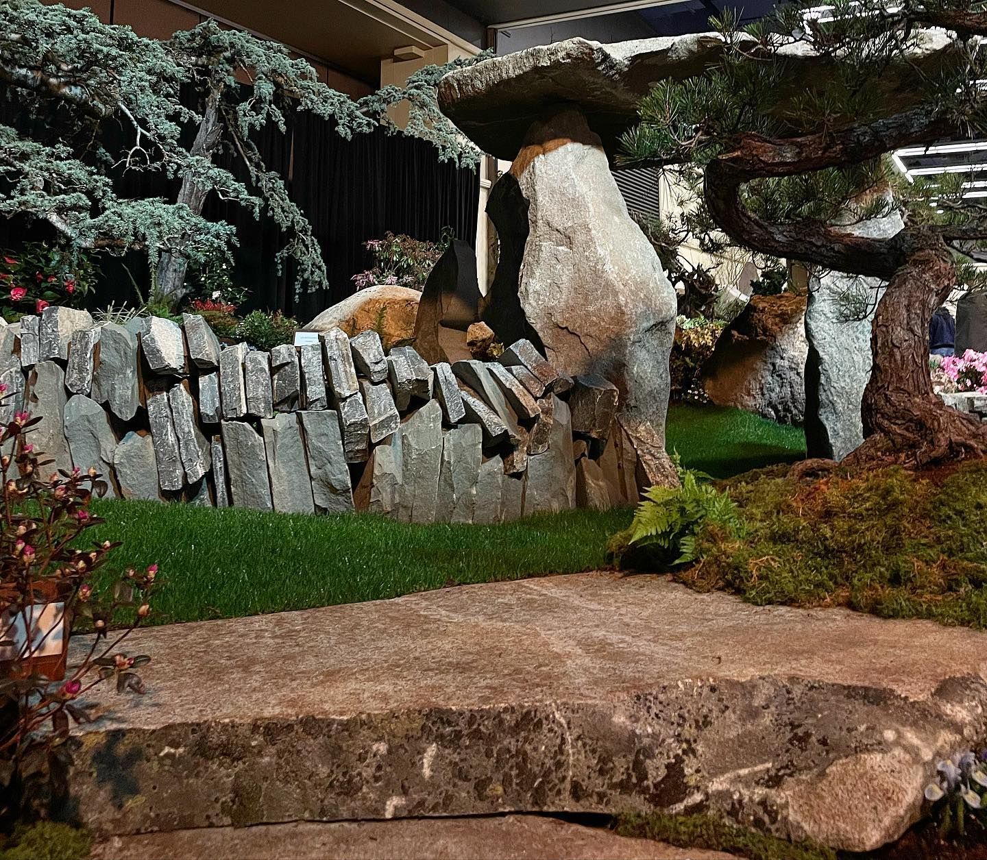 Rock garden with stone wall, mossy greenery, and large boulders beneath a covered patio.