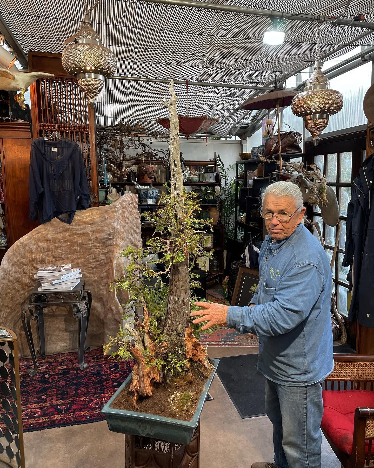 Man adjusting a tall floral arrangement in a decorative shop with hanging lanterns and rugs