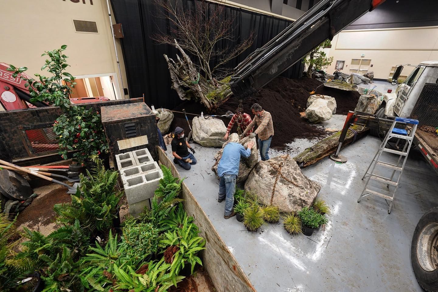 People arranging rocks and plants in a lobby garden beside a large black staircase