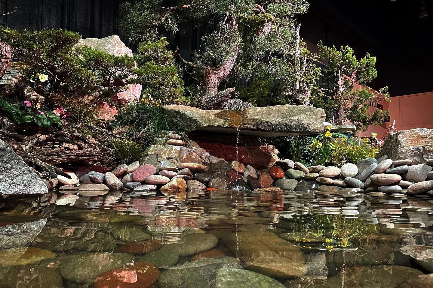 Koi pond with stone waterfall, rocks, and lush garden plants at dusk