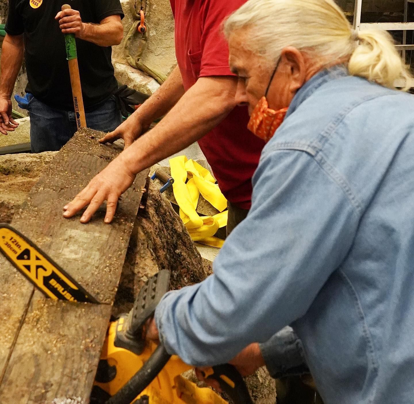People using shovels to dig in muddy ground near a yellow tool