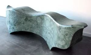 Sculptural stone-like bench with a wavy, curved surface in a gallery setting