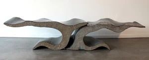 Abstract gray sculpture on a tabletop with flowing, layered curves and a central arch opening