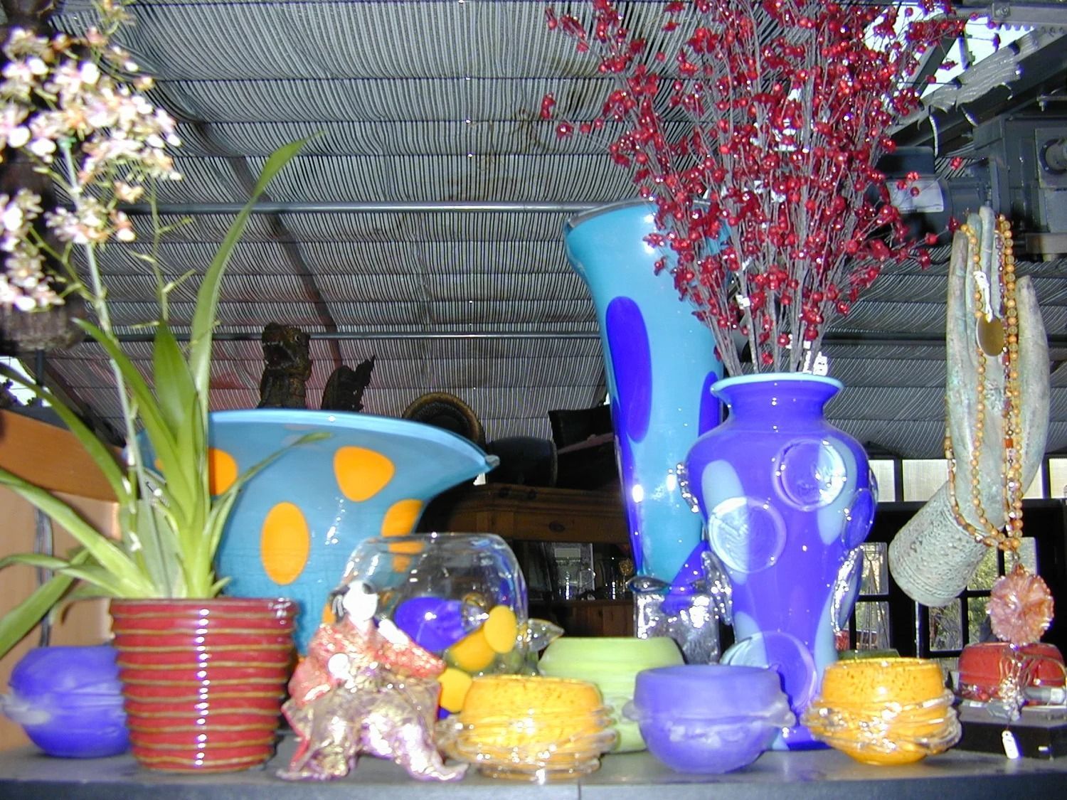 Colorful ceramic vases and decorative bowls arranged on a table with flowers and branches in a shop display