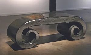 Abstract dark metal bench with curled scroll-like ends on a gray floor.