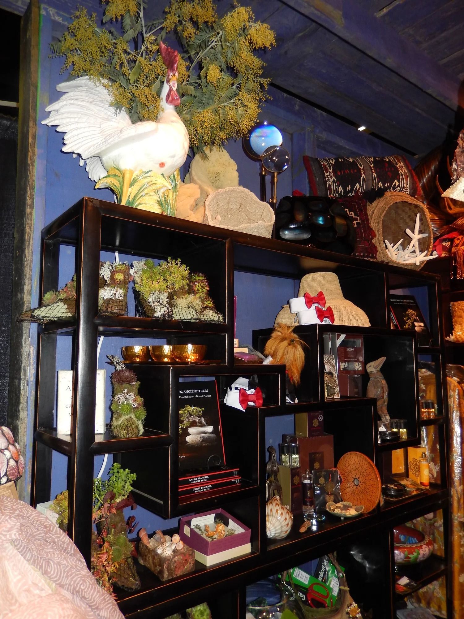 Shelves of decorative items in a shop, topped with a white bird sculpture and yellow flowers.