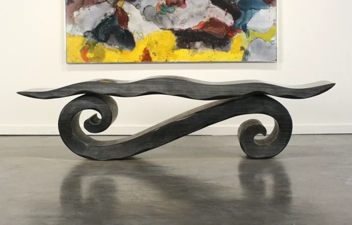 Abstract dark metal bench with curled ends in a gallery, beneath a colorful painting on a white wall