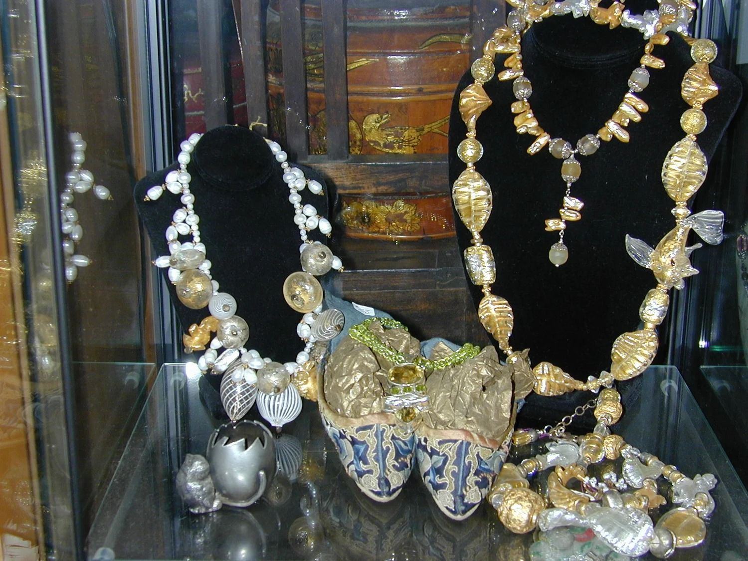 Display case with ornate gold and silver necklaces on black busts and a decorative jeweled purse