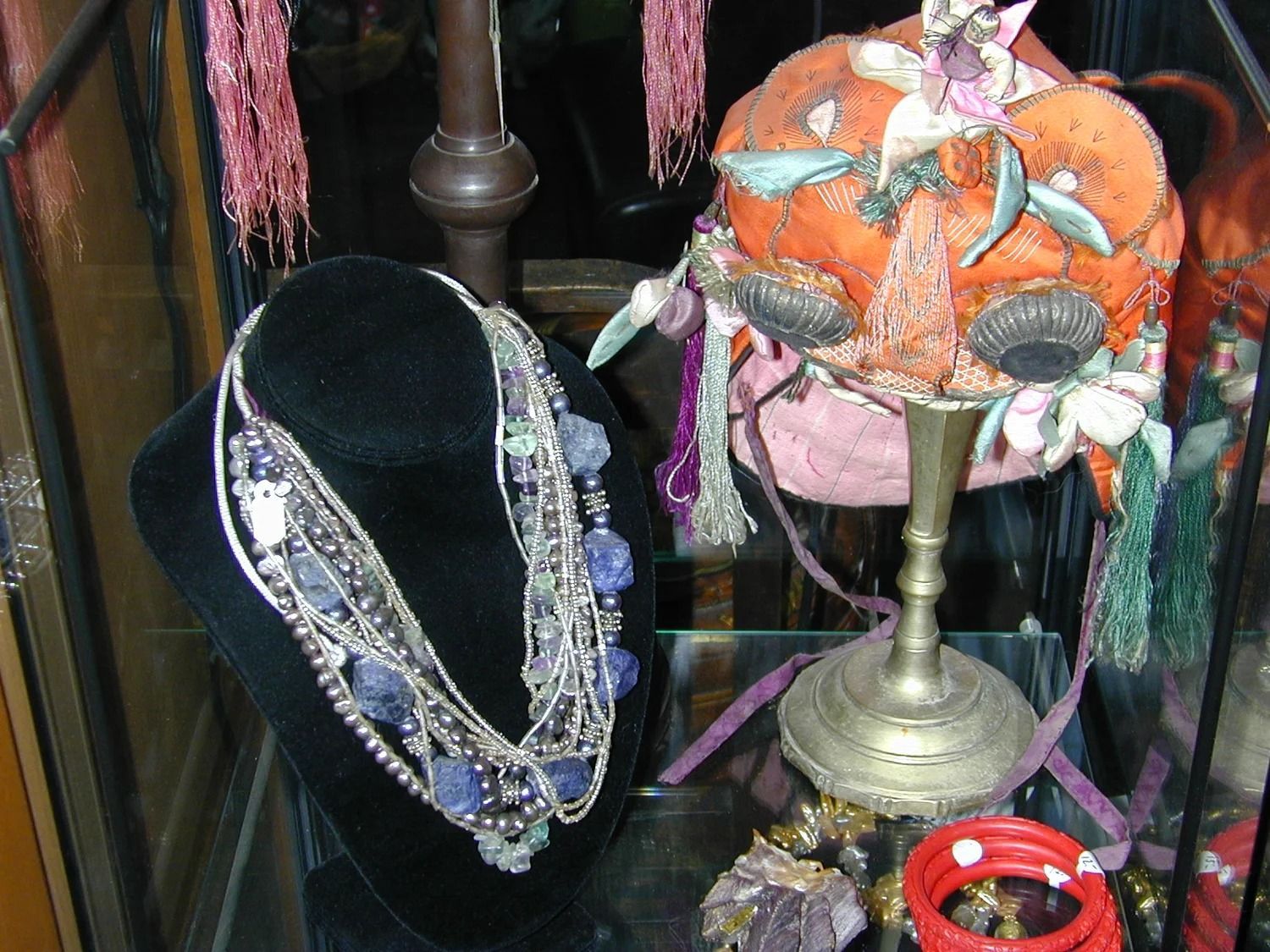 Black necklace display beside orange-and-pink hats on stands with colorful hanging scarves