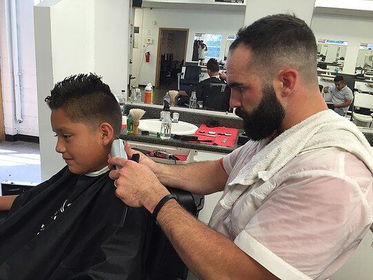 A man with a beard is cutting a boy 's hair in a barber shop.