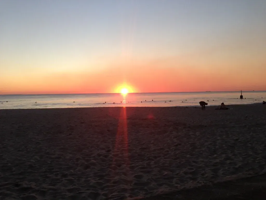Sunset over a sandy beach with silhouettes of people near the waterline