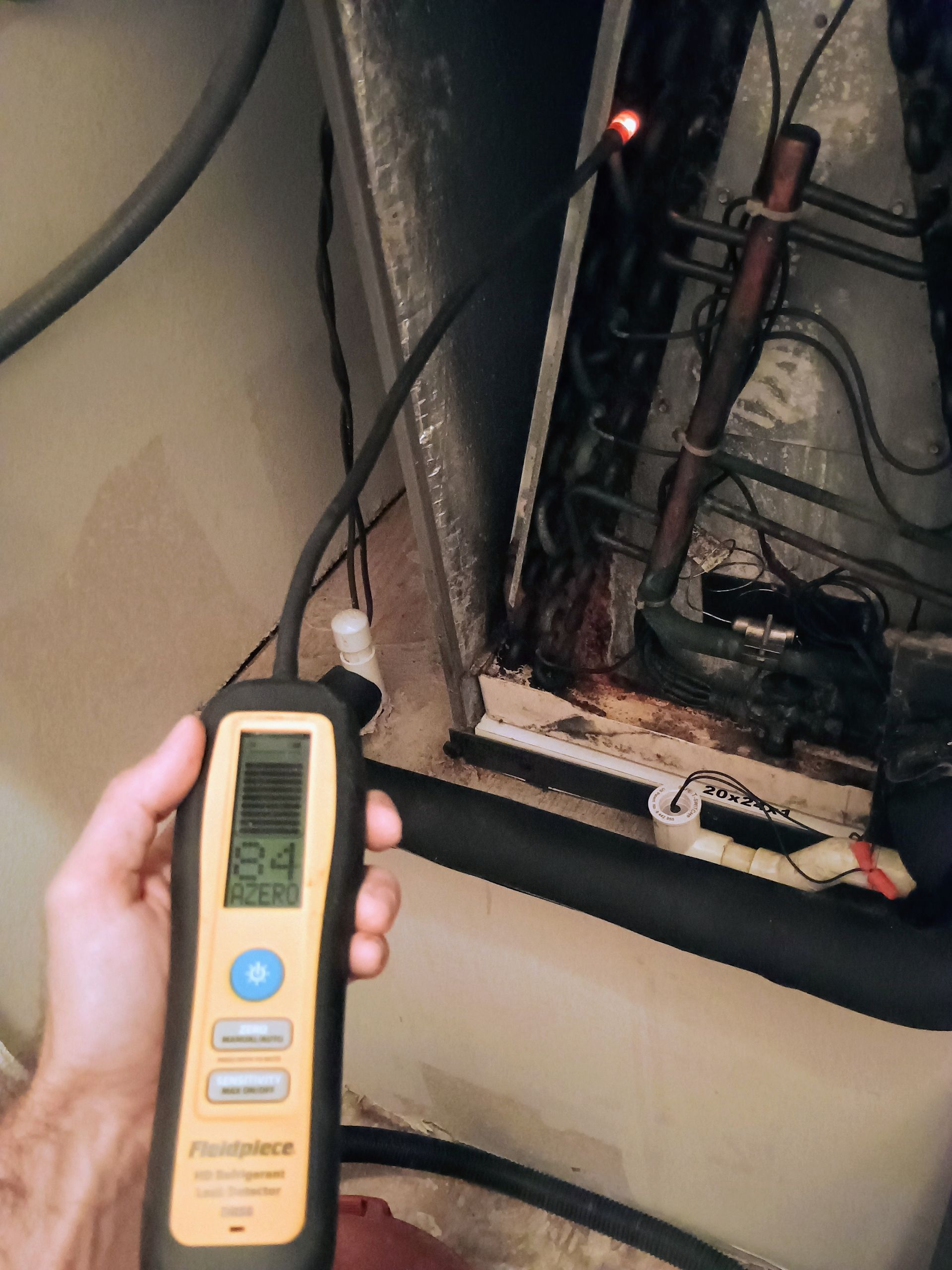 Hand holding a refrigerant leak detector probe inside an air handler unit, displaying a reading.