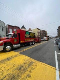 Red truck with trailer parked in a street, yellow crosswalk, buildings in the background.