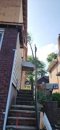 Exterior stairs leading to a house, flanked by brick and siding. A mailbox is visible. Overcast sky.