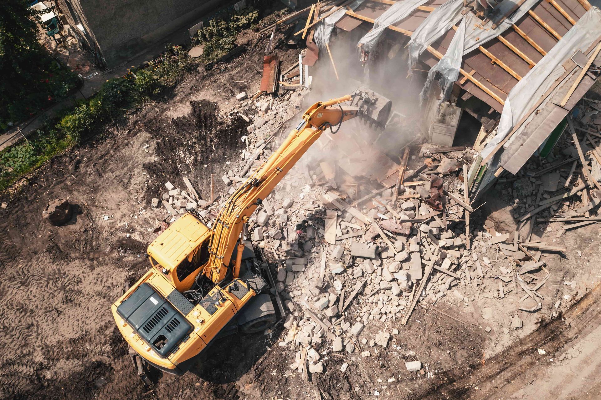 Yellow excavator demolishing a collapsed building amid rubble and dust