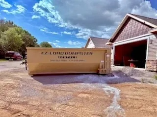 A row of dumpsters are parked in a gravel lot.