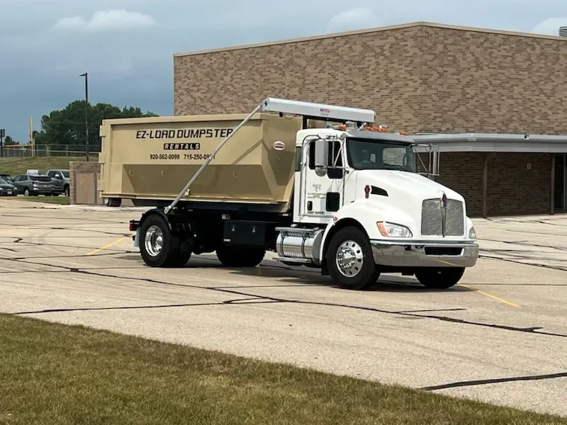 A dumpster is sitting in a gravel lot next to a truck.