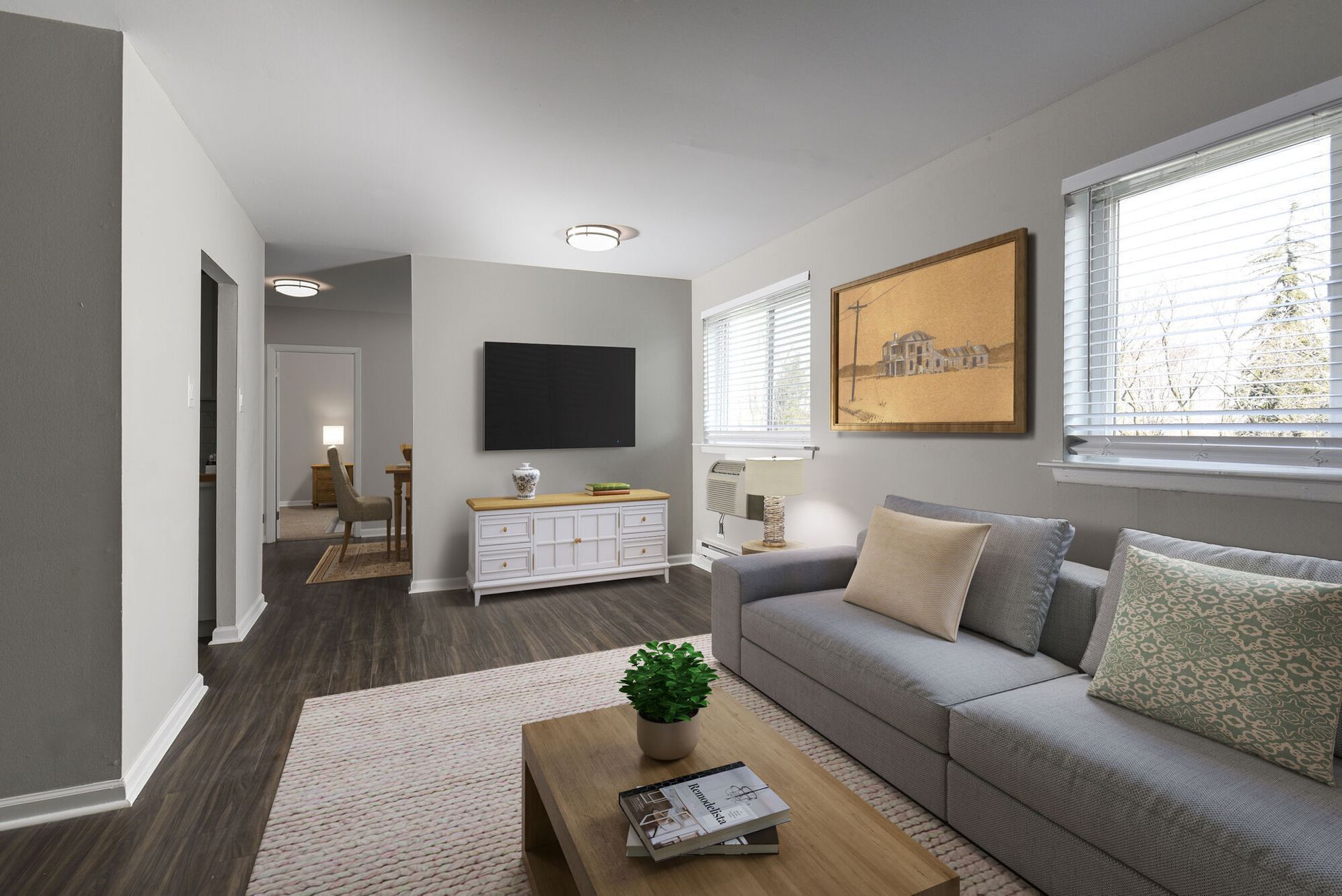 Interior living room with gray sofa, coffee table, wall-mounted TV, and large windows at The Addison, offers townhomes in North Wales, PA.