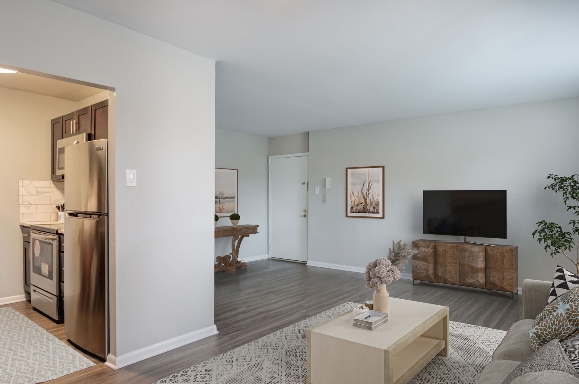 Open-concept living room with a sofa, coffee table, and a TV; kitchen is visible on the left at The Addison, offers townhomes in North Wales, PA.