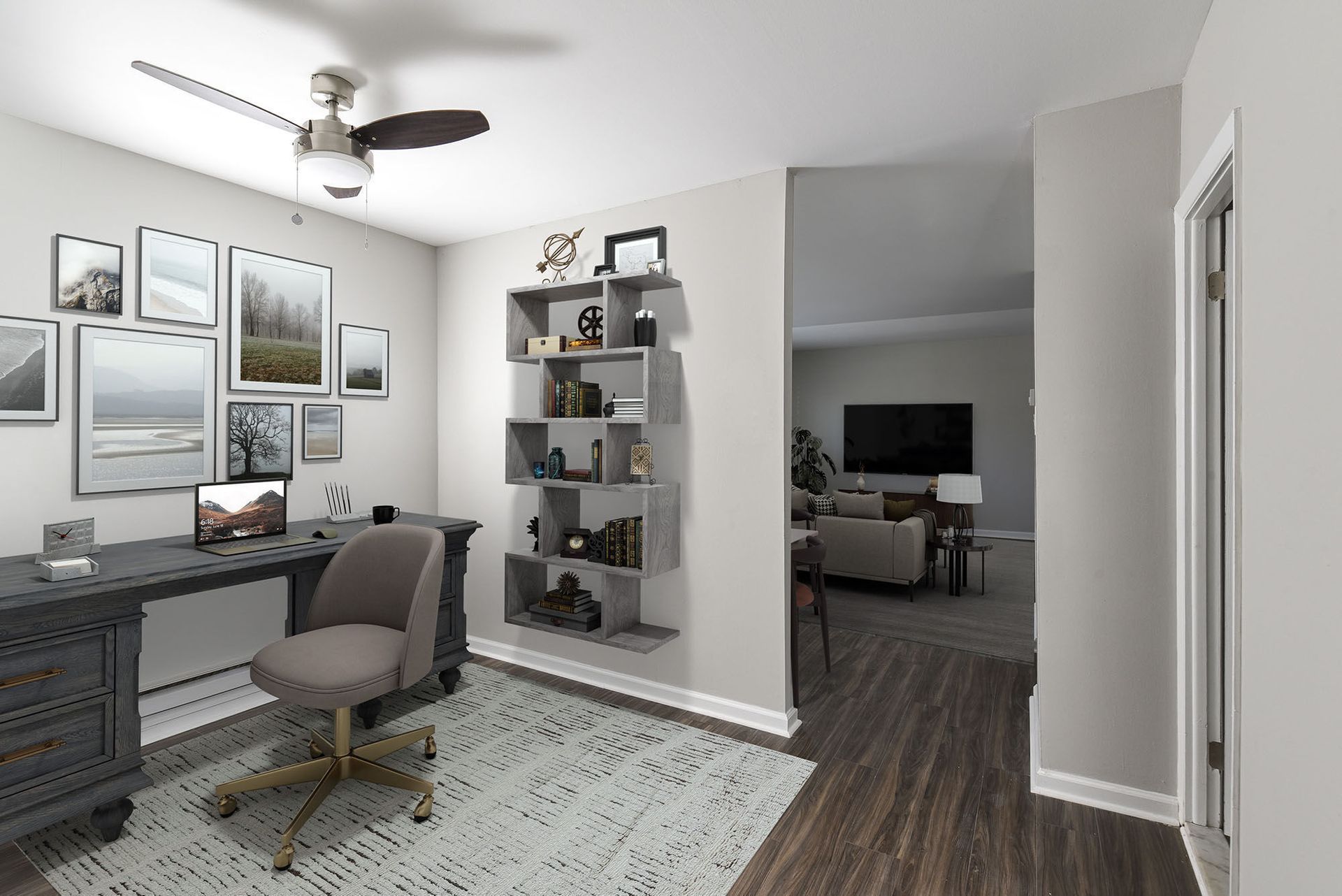 Home office with a gray desk, swivel chair, wall shelves, and an entry to the living room at The Addison, offers apartments for rent in North Wales near Gwynedd Mercy University.