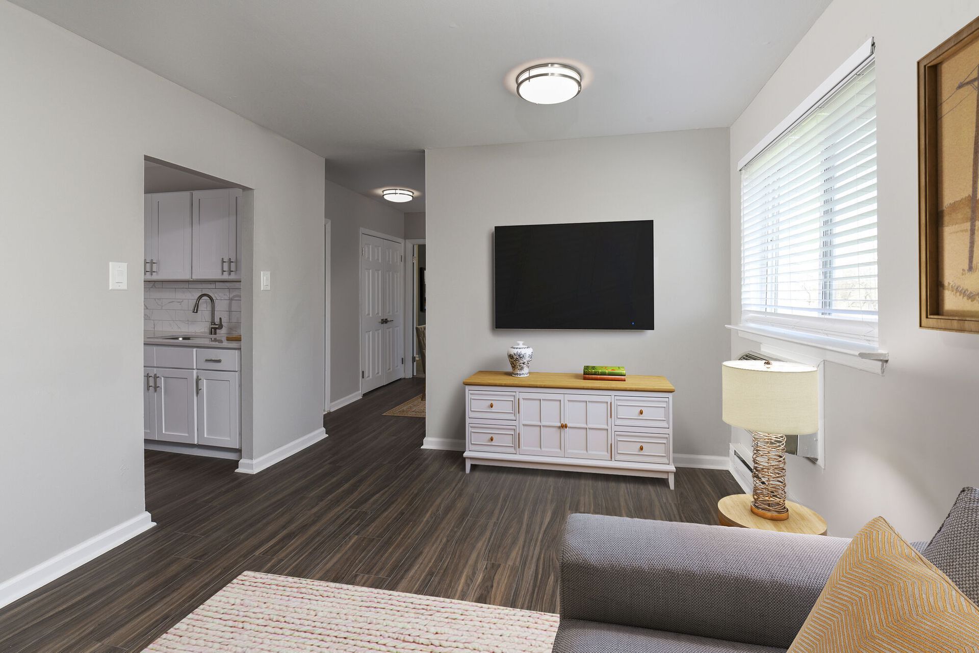 Living room with wall-mounted TV, white media console, and window blinds at The Addison, offers townhomes in North Wales, PA.