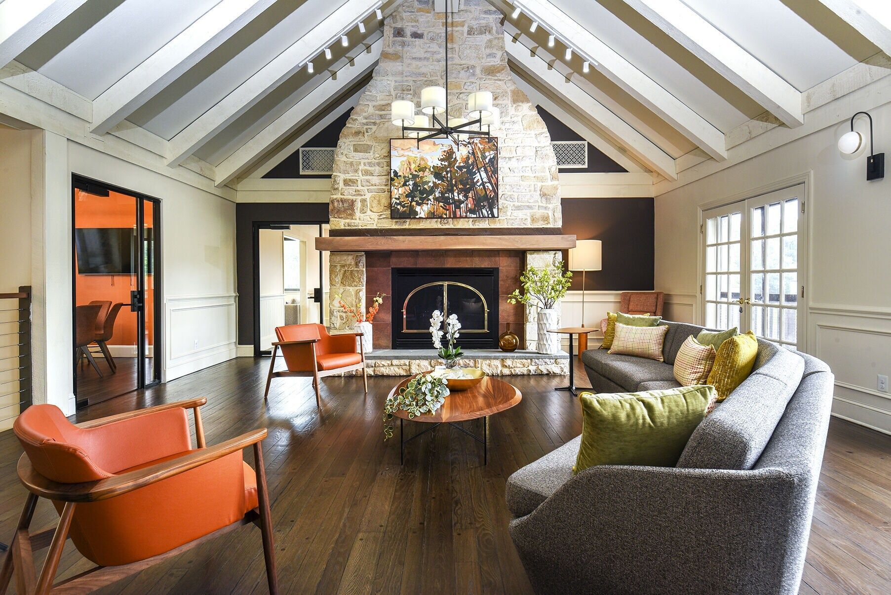 Bright living room with a stone fireplace, vaulted white-beamed ceiling, and orange chairs at The Addison, offers townhomes for rent in North Wales, PA.