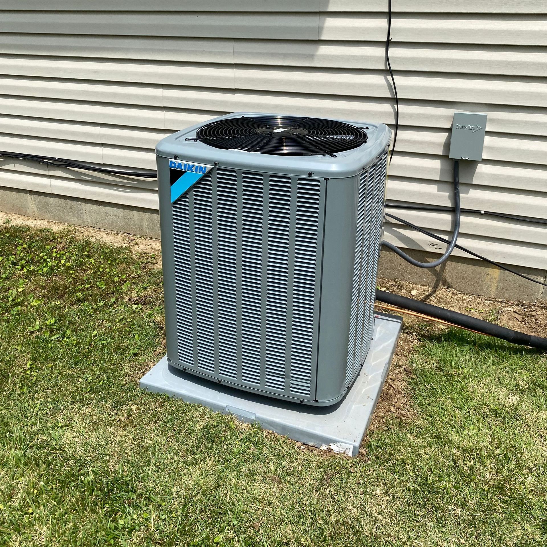An air conditioner is sitting on top of a concrete platform in front of a house.