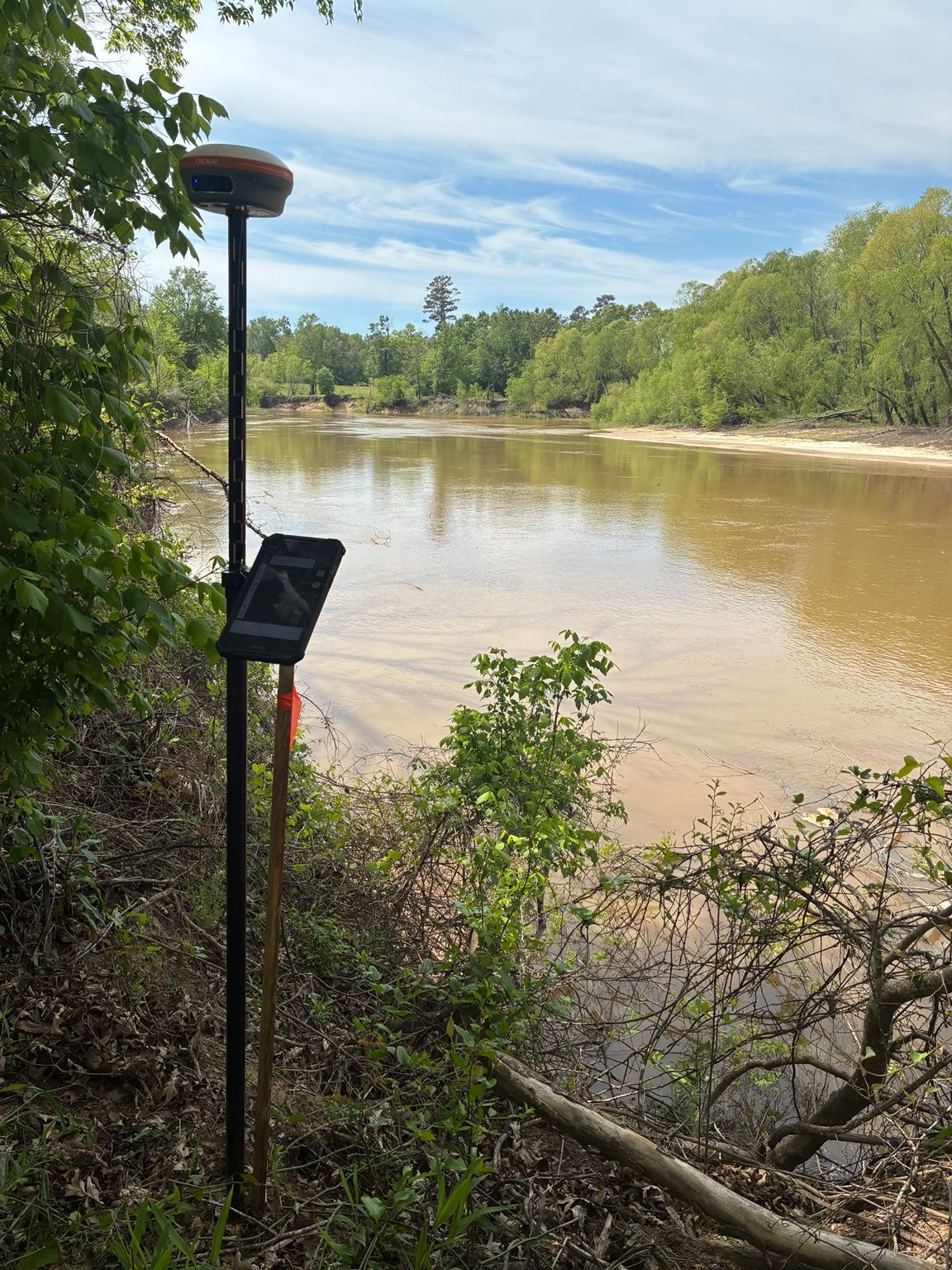 GNSS survey equipment beside a wooded riverbank