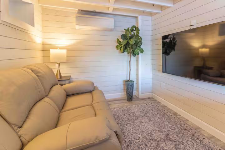 Modern living room with beige sectional, wall-mounted TV, floor lamp, and potted plant