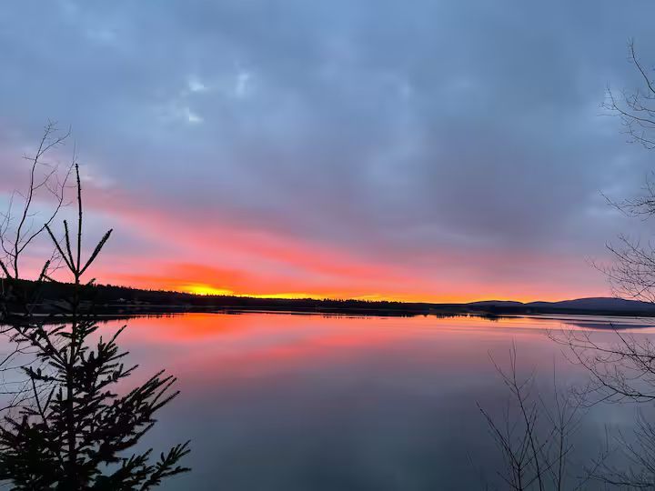 Sunset over a calm lake with pink and orange reflections beneath a cloudy blue sky