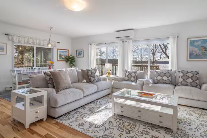 Bright living room with gray sofas, white coffee table, patterned rug, and large windows with natural light