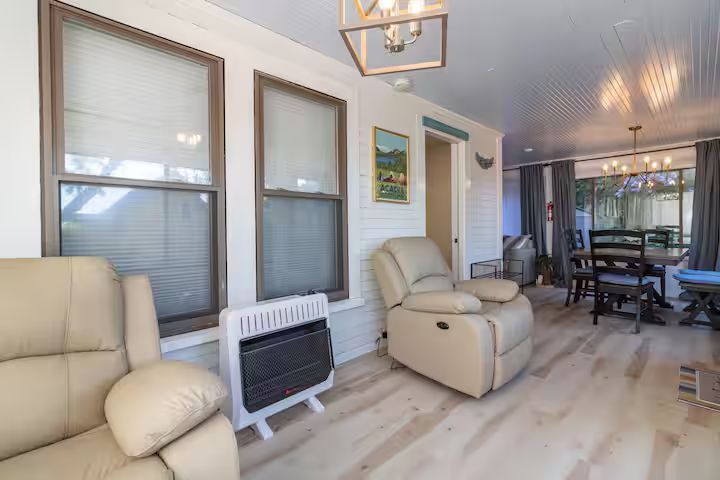 Bright living room with cream recliners, windows, and a dining area in the background