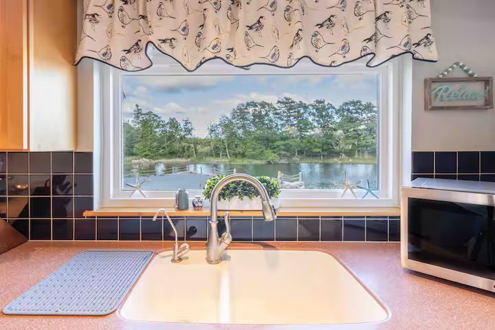 Kitchen sink under a window overlooking a lake, with dark tile, microwave, and floral valance.
