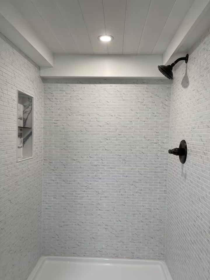 Empty white-tiled shower stall with two black showerheads and a ceiling light