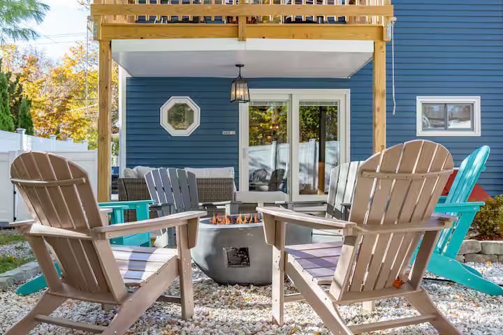 Backyard patio with Adirondack chairs around a fire pit outside a blue house