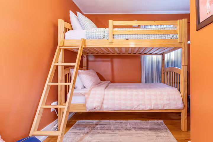 Orange bedroom with a wooden bunk bed, ladder, striped bedding, and a rug underneath
